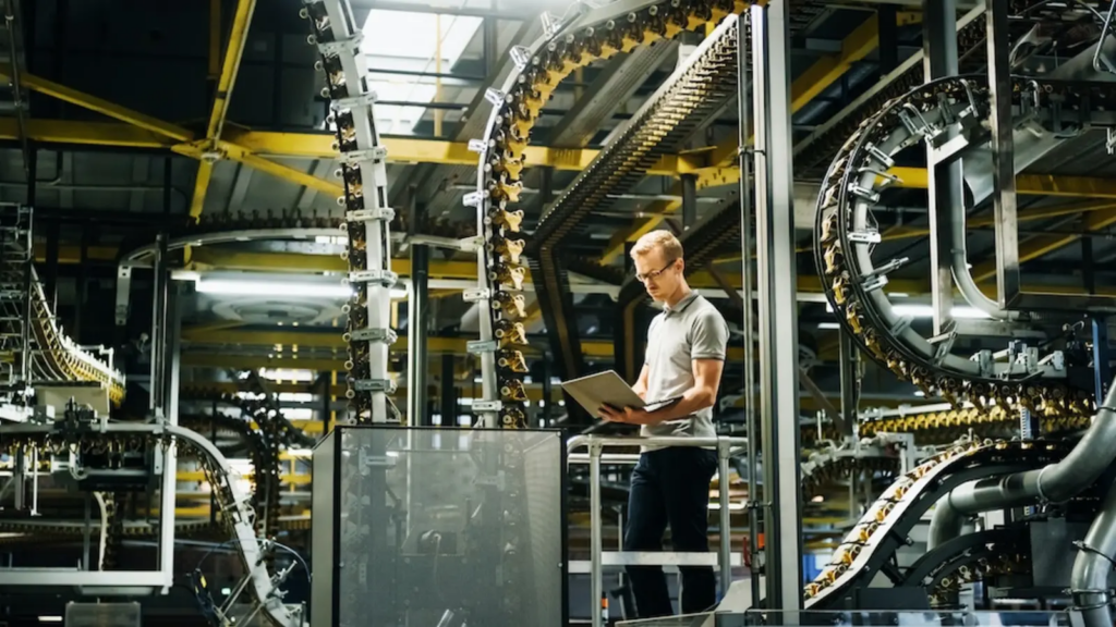 A man working on his laptop in a robotic facility. (Image Source | Unplash)